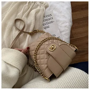 Macro detail of beige quilted bucket bag with golden interlocking clasp and chain strap