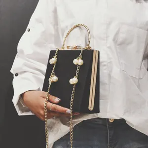 Detail of black leather clutch bag with gold round handle and oversized pearl strap