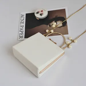 Close-up of white square handbag featuring gold frame and faux pearl chain strap detail