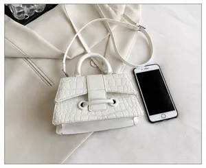 Handtasche mit Krokodilmuster und Smartphone als Größenvergleich auf beigem Sakko