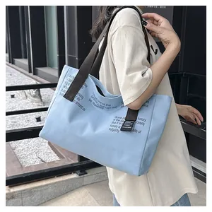Détail du grand sac cabas en toile bleu clair avec anses marron porté à l'épaule