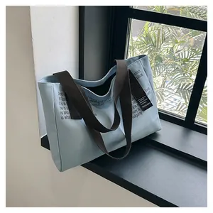 Détail d'un sac cabas en toile bleu clair avec des anses brunes sur un rebord