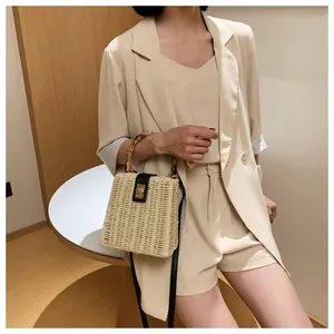 Detail of woven straw box bag featuring a bamboo handle and sleek gold metal clasp