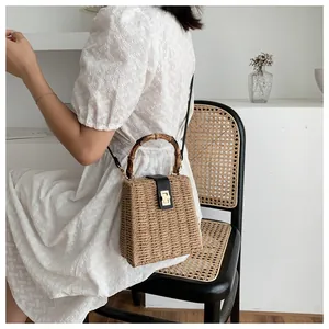 Detail of woven straw box bag featuring bamboo handle and black leather flip cover