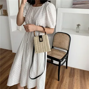 Handcrafted woven straw box bag with bamboo handle and leather strap for a chic summer look
