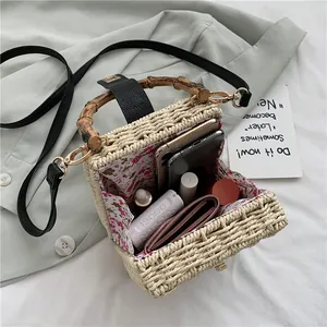 Handwoven straw box bag with bamboo handle and floral lining, includes crossbody strap