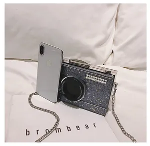 Macro detail of camera shaped glitter clutch with silver chain on white bedding