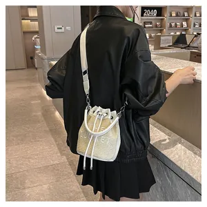 Model wearing straw bucket bag with white leather trim and THE BUCKET embroidery detail
