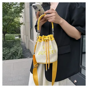 Detail of woven straw bucket bag with yellow leather trim and THE BUCKET embroidery