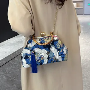 Blauwe retro handtas met kraanvogelprint, bamboe handvat en kwastjes op beige jas