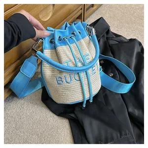 Detail of a straw bucket bag featuring blue embroidery text and leather drawstring closure