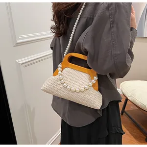 Detail of straw handbag featuring U-shaped wooden handle and elegant large pearl strap