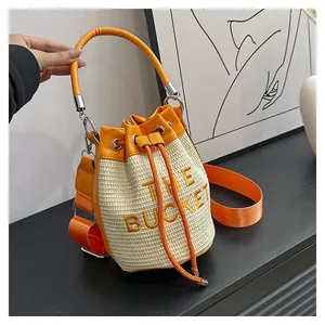 Detail of woven straw bucket bag featuring orange drawstring closure and embroidered text