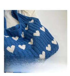 Close-up detail of blue knitted shoulder bag with white heart pattern and cable texture