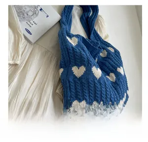 Detail of blue knit shoulder bag with white heart patterns and chunky cable knit texture