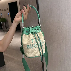 Fashionable straw bucket bag in green and beige featuring embroidered letters and wide strap