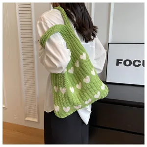 Detail of green knitted shoulder bag with white heart patterns in a spacious tote style