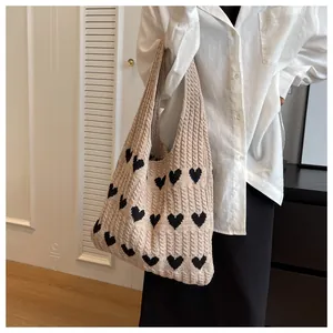 Side view of a large cream knitted tote bag with black heart patterns on a female model