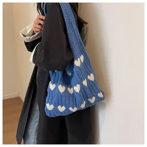 Detail view of blue knitted shoulder bag with white heart patterns and soft woven texture