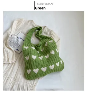 Close-up of green knitted tote bag with white heart pattern on a cream dress