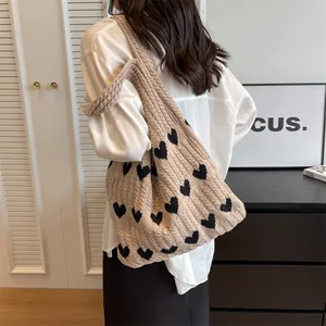 Beige knit tote bag with black heart patterns shown on model's shoulder for casual use