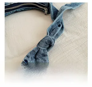 Detail of the knotted handle design and silver zipper on this blue denim shoulder bag