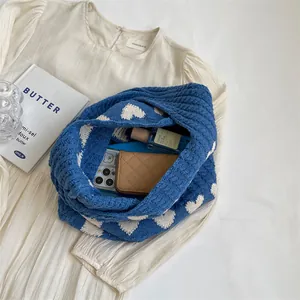 Blue knit shoulder bag with white hearts shown with daily essentials on fabric