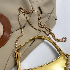 Dettaglio mini borsa dorata lucida con tracolla a catena e grande perla decorativa