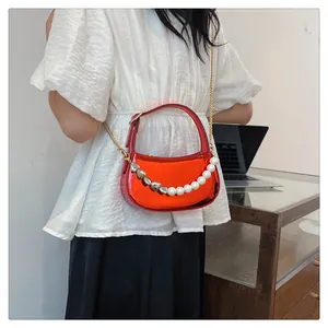 Dettaglio di borsa a mezzaluna rossa metallizzata con manico di perle e cuori su modella