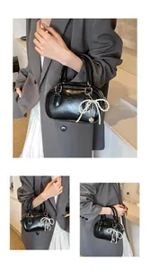 Detail of black glossy PU handbag with pearl bow and heart charm on double handles