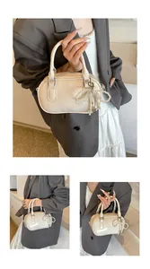 Detail view of cream Boston handbag with pearl bow charm and soft leather texture