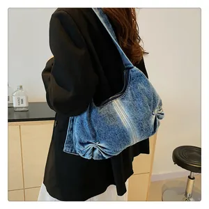Detail shot of washed blue denim shoulder bag featuring ruched texture and metal zipper