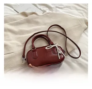 Detail view of burgundy PU leather handbag with white pearl bow charm on soft fabric