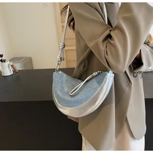 Detail of hobo bag showing blue denim texture, metallic silver base and knot strap