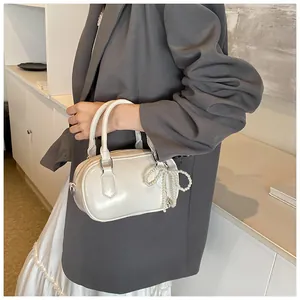 Detail of creamy white Boston bag featuring a pearl bow charm and glossy finish