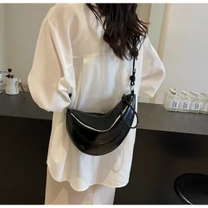 Detail of glossy black crescent shoulder bag with knotted strap on white shirt model