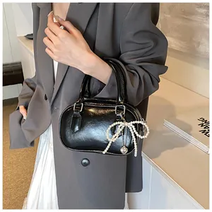 Detail of glossy black handbag with pearl bow and heart charm held by a model