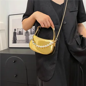 Borsa a mano dorata a mezzaluna con manico di perle su modella in abito nero