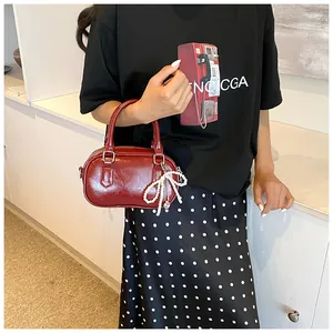 Detail of burgundy PU leather handbag featuring a white pearl bow charm and heart pendant