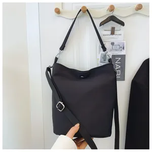 Detail of a minimalist black bucket bag with metallic snap closure and adjustable strap