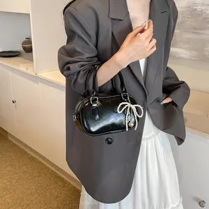 Minimalist black shiny bowling handbag with pearl bow charm and crossbody strap
