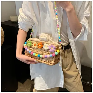 Detail of woven straw crossbody bag featuring colorful crochet flowers and beaded strap