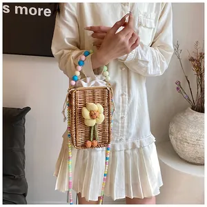 Detail of hand-woven straw crossbody bag with floral ornament and colorful beaded strap