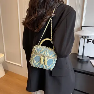 Frayed denim vanity bag with yellow leather handle and chain strap worn over black suit