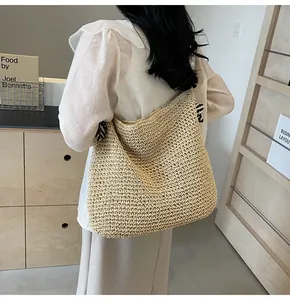 Detailed side view of a large beige woven straw shoulder bag worn by a model
