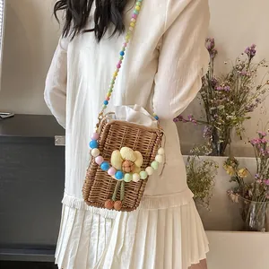 Straw crossbody bag with floral detail and colorful beaded strap worn by a model