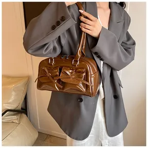 Brown patent leather bowling bag with bow pockets shown on shoulder of stylish blazer outfit