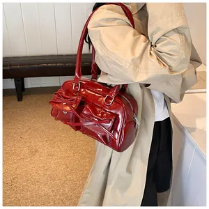 Red glossy bowling bag featuring side pockets and bow ties shown on a beige coat