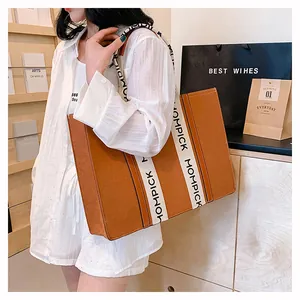 Detail of a brown leather tote bag with a wide white branded strap shown on a model