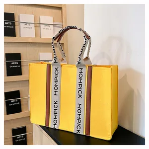 Detail of yellow felt tote bag with gray logo handles and brown leather accents